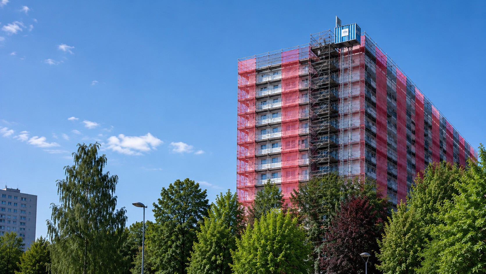 Flerbostadshus under renovering med byggställning och skyddsduk på fasaden.